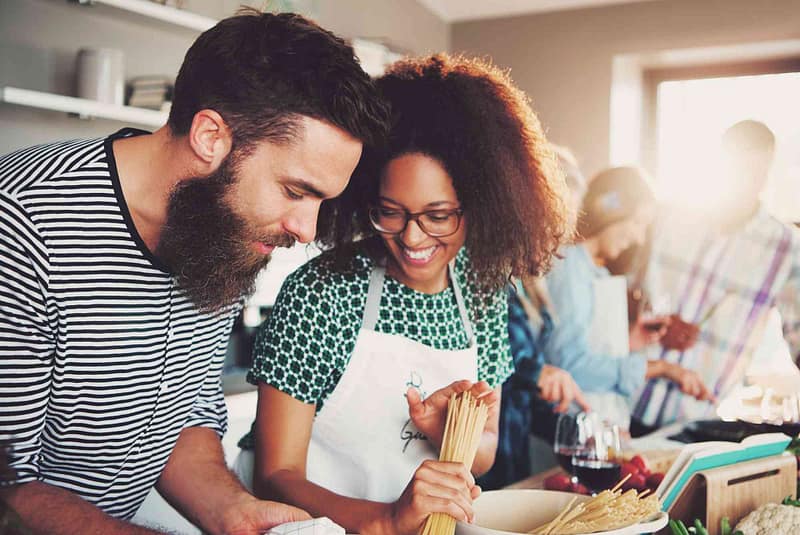 Couple making pasta dinner in kitchen with friends